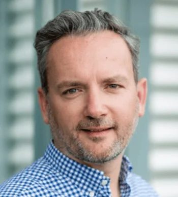 Thorsten Vortmeyer mit grauen Haaren und Bart, in einem karierten Hemd, lächelt in die Kamera.